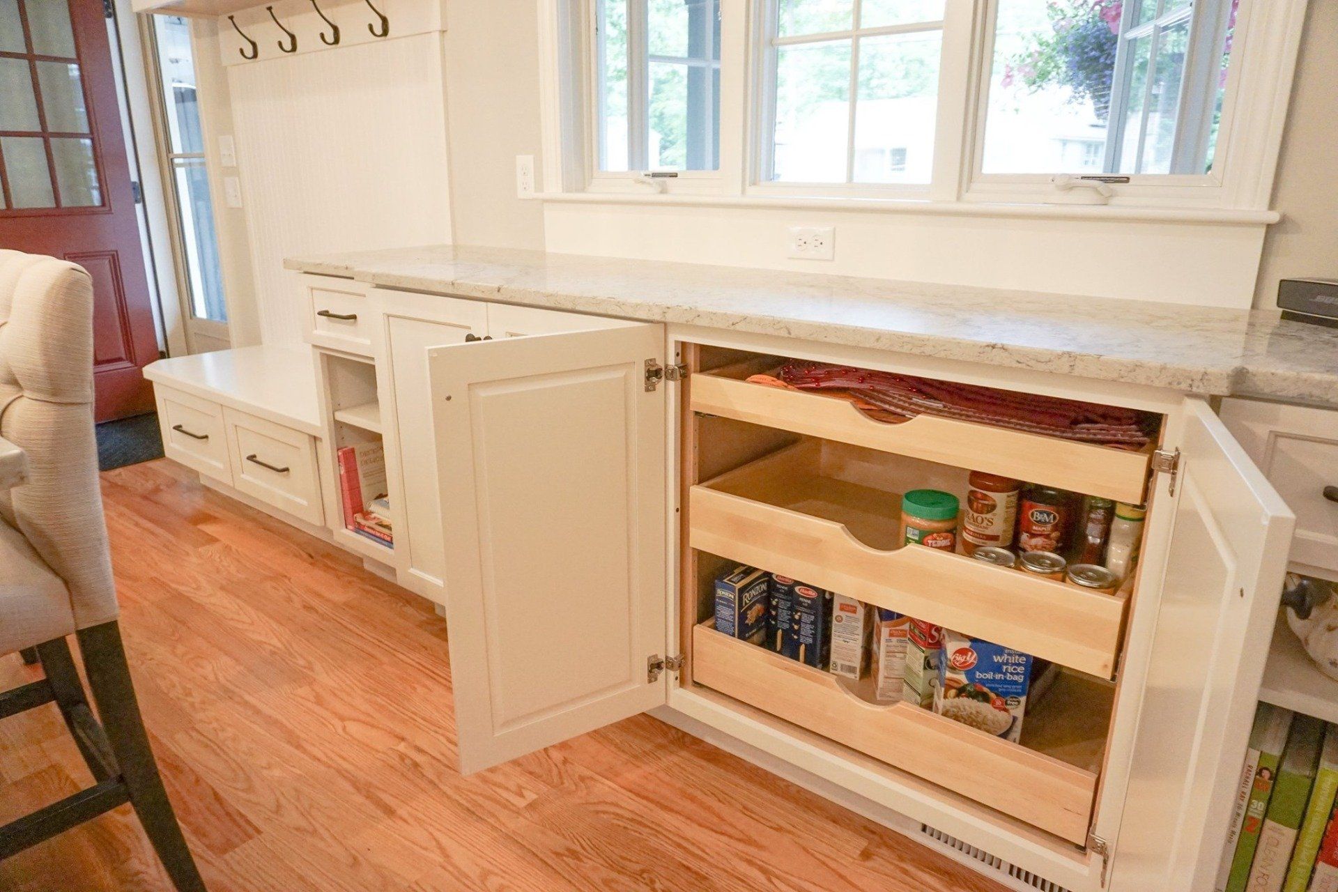 A kitchen with white cabinets and wooden drawers filled with food.