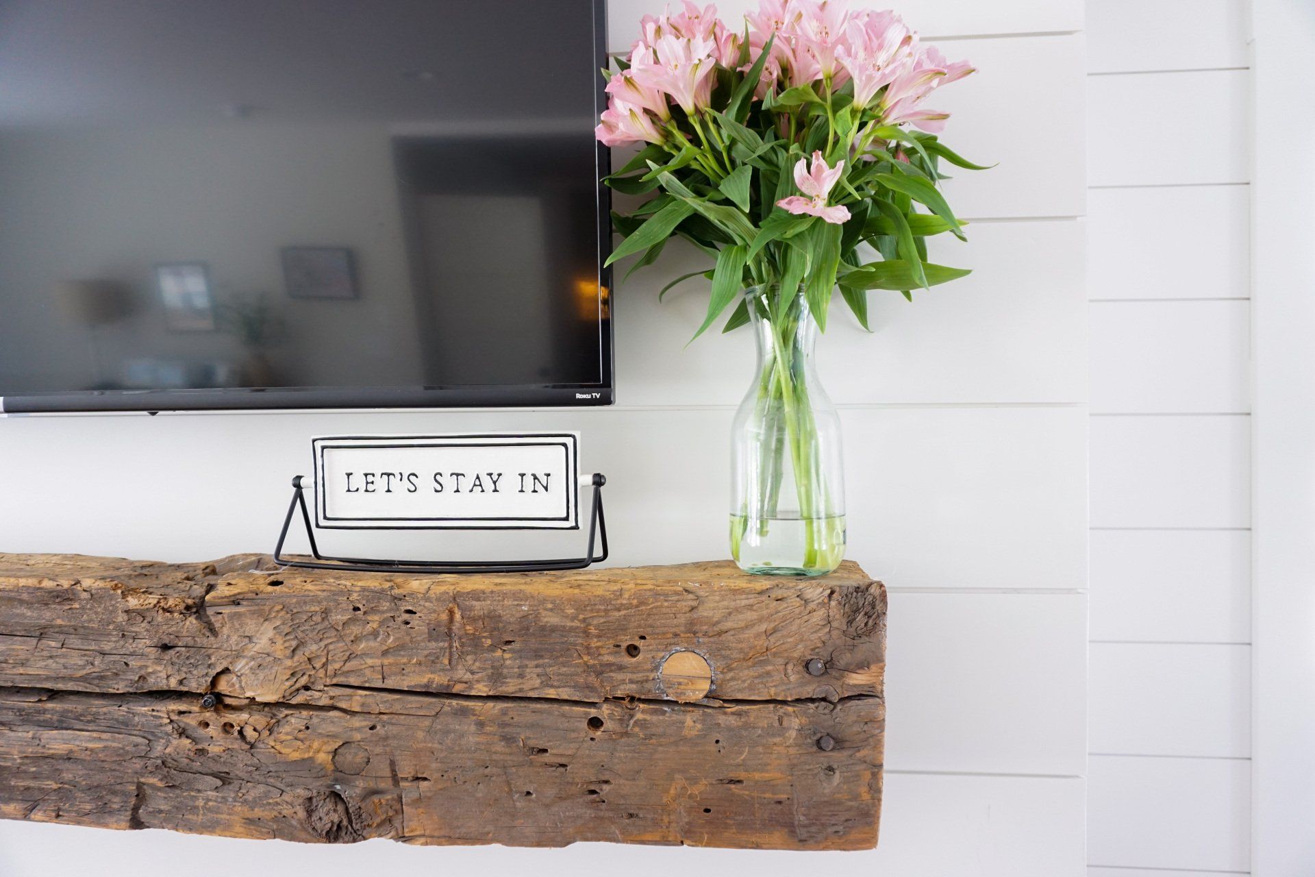 A vase of flowers is sitting on a wooden shelf next to a television.