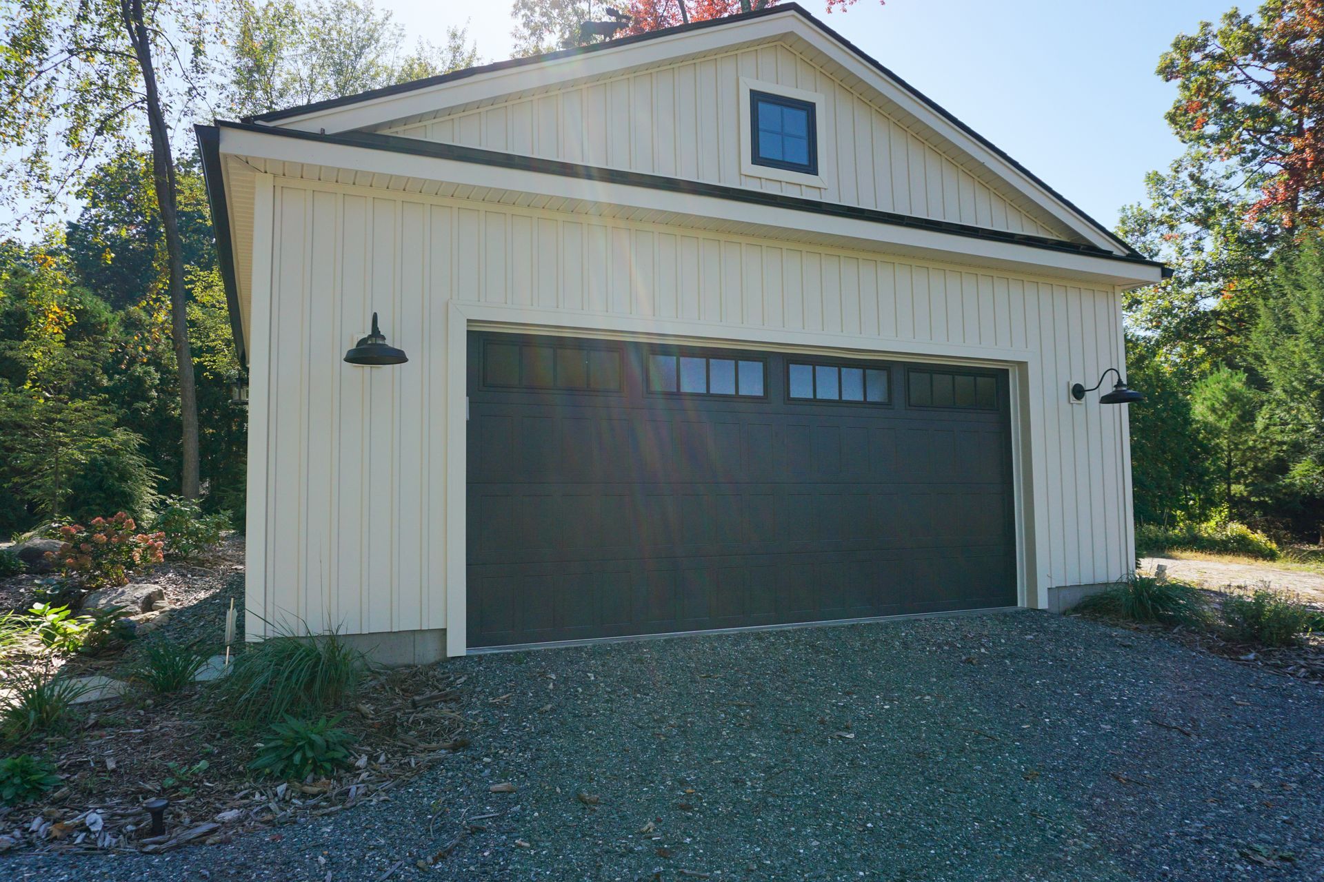 A white garage with a black garage door is sitting on top of a gravel driveway.