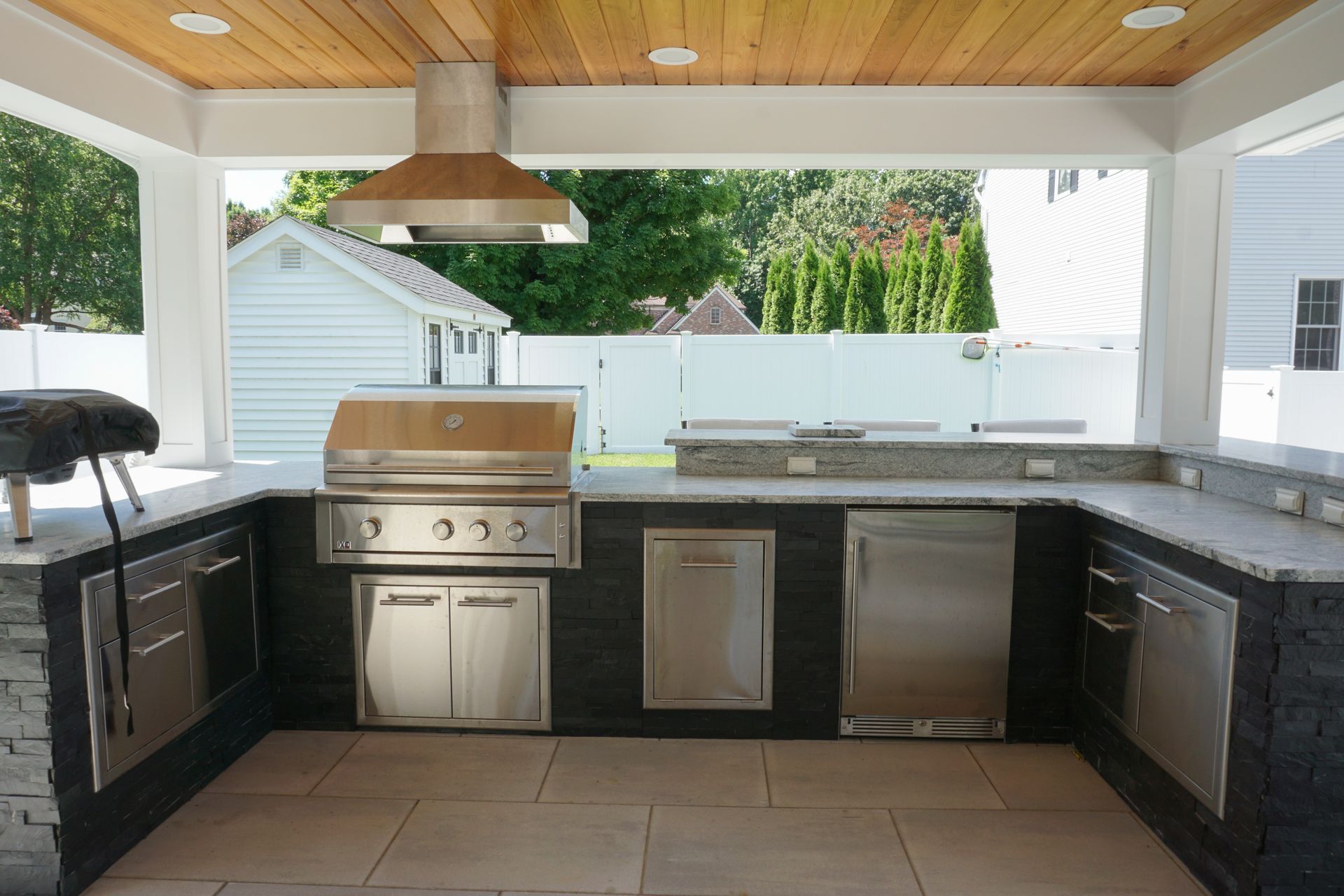 Outdoor kitchen with stainless grill, sink, and cabinets under a wood-paneled roof