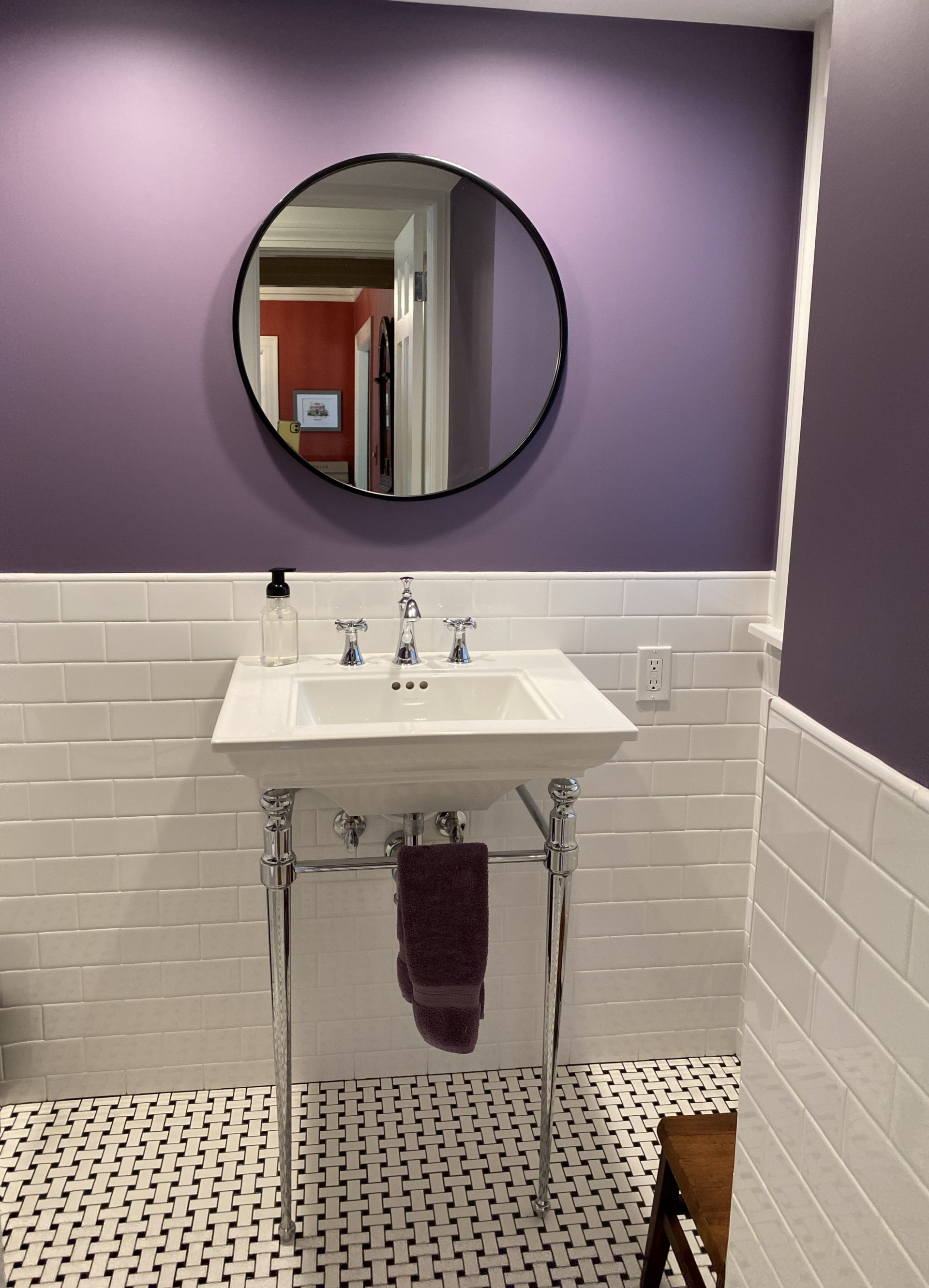 a bathroom with purple walls , white tiles , a sink and a mirror .