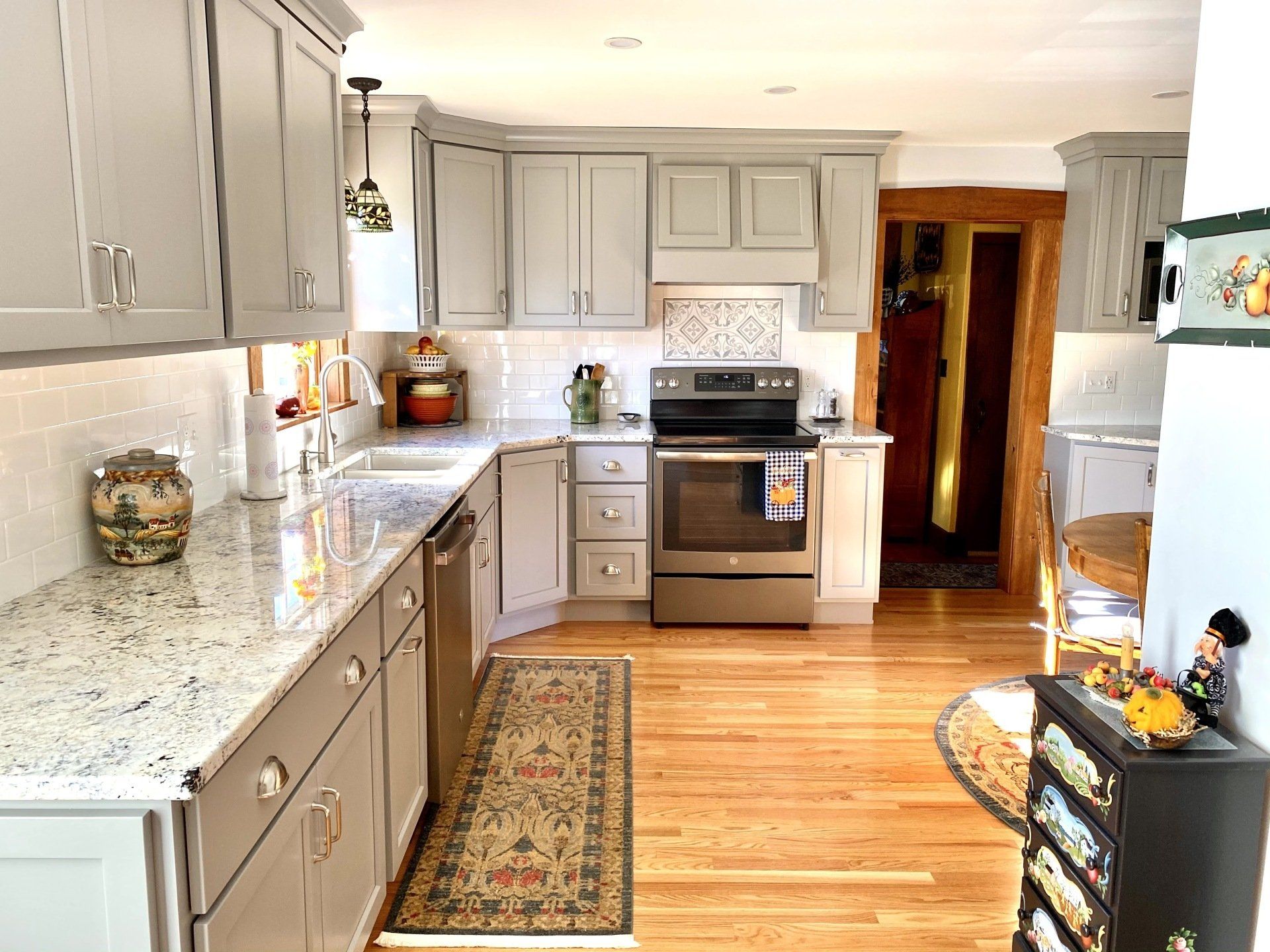 A kitchen with gray cabinets , granite counter tops , stainless steel appliances , and hardwood floors.