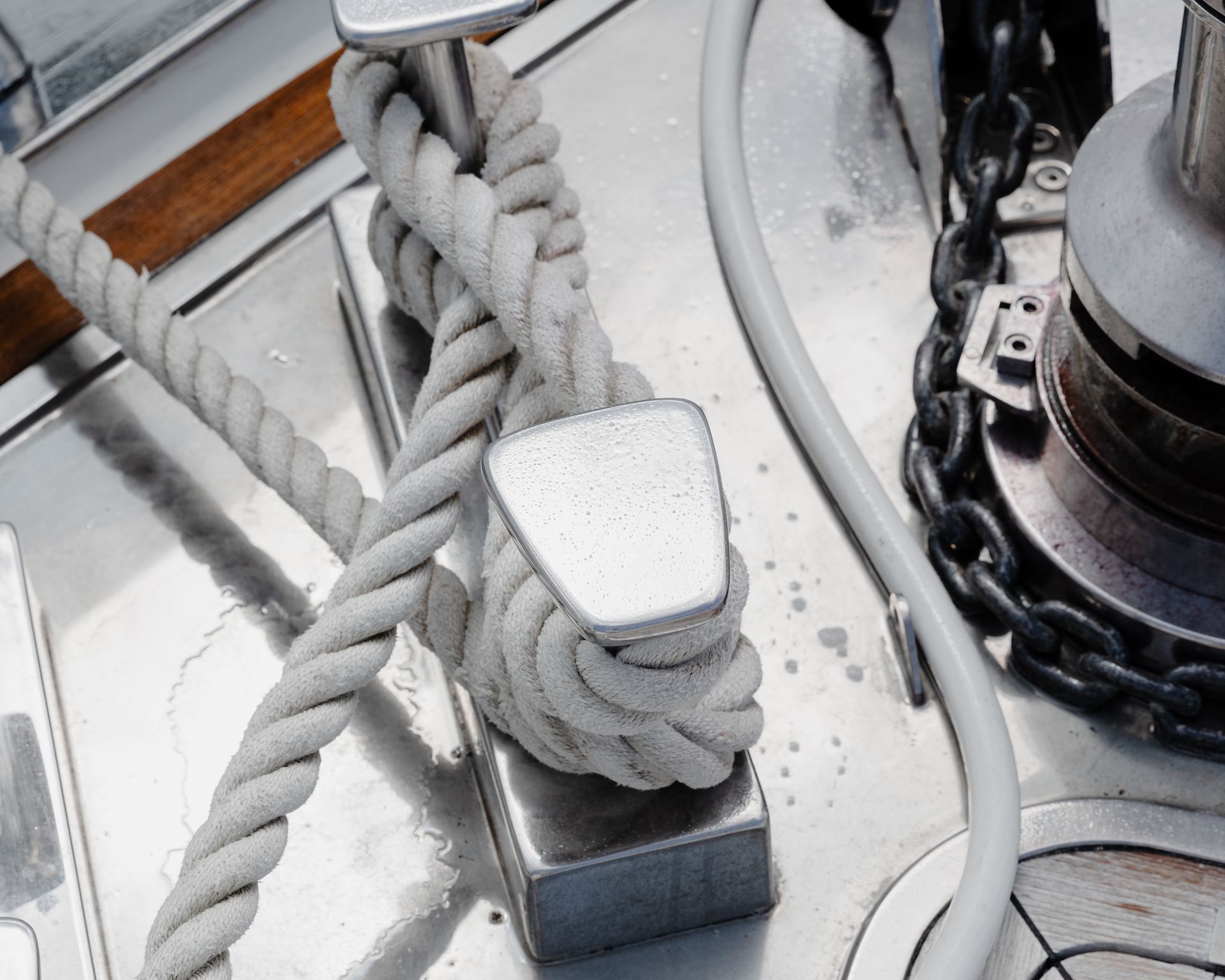 Coiled white rope on a metal boat cleat beside a chain and deck hardware