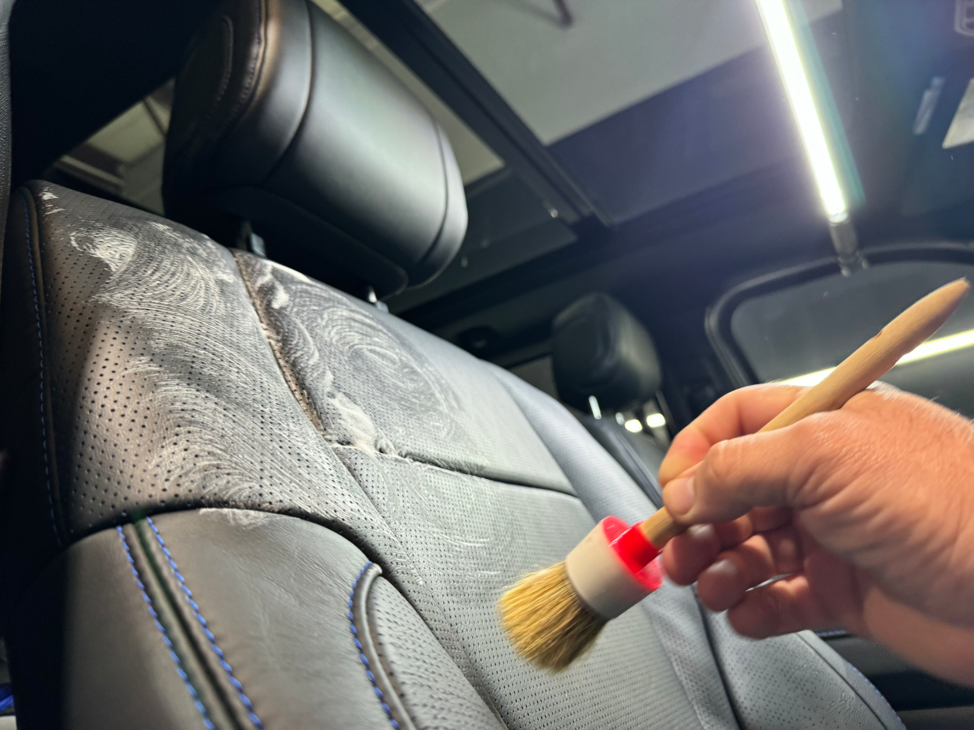 A person is cleaning the back seat of a car with a brush.