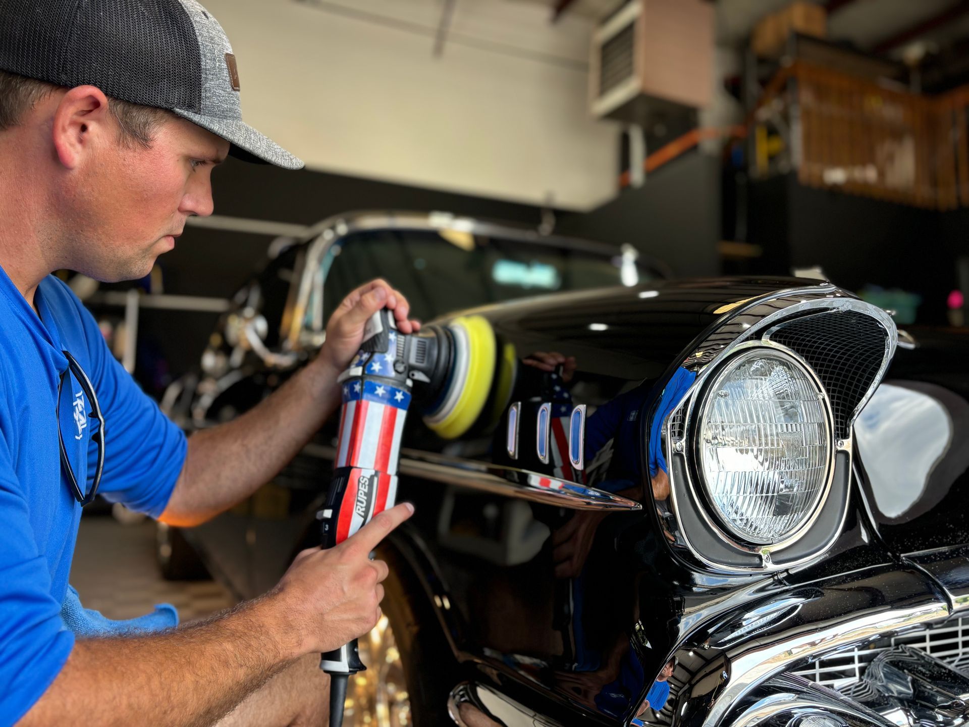 A man is polishing a black car in a garage.