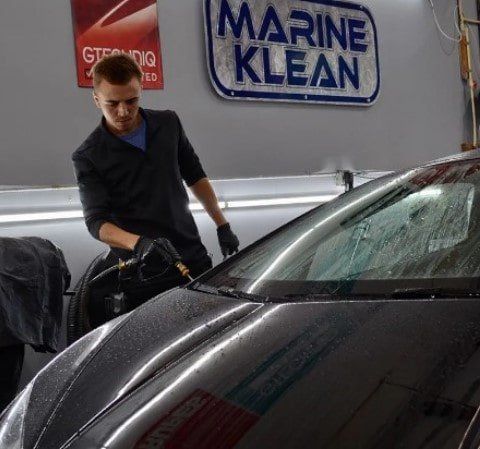A man is washing a car in front of a marine klean sign