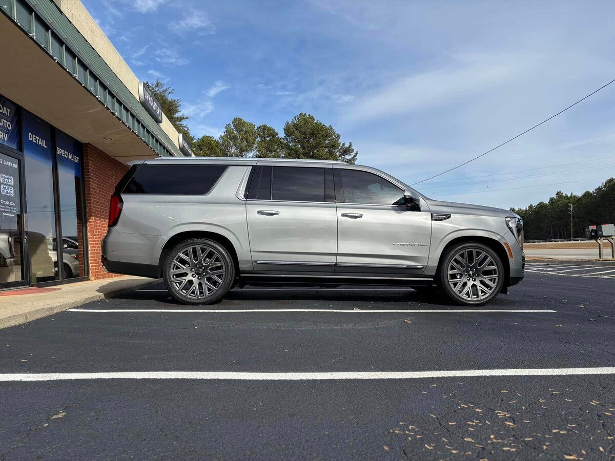 A silver GMC Yukon XL SUV parked outside a building with tinted windows under a partly cloudy sky.