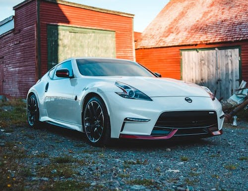 A white sports car is parked in front of a red barn.