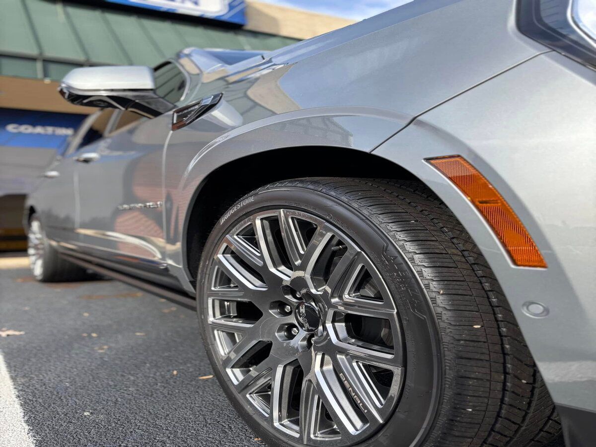 Close-up of a silver SUV with chrome wheels parked on an asphalt surface. The car has amber side markers.