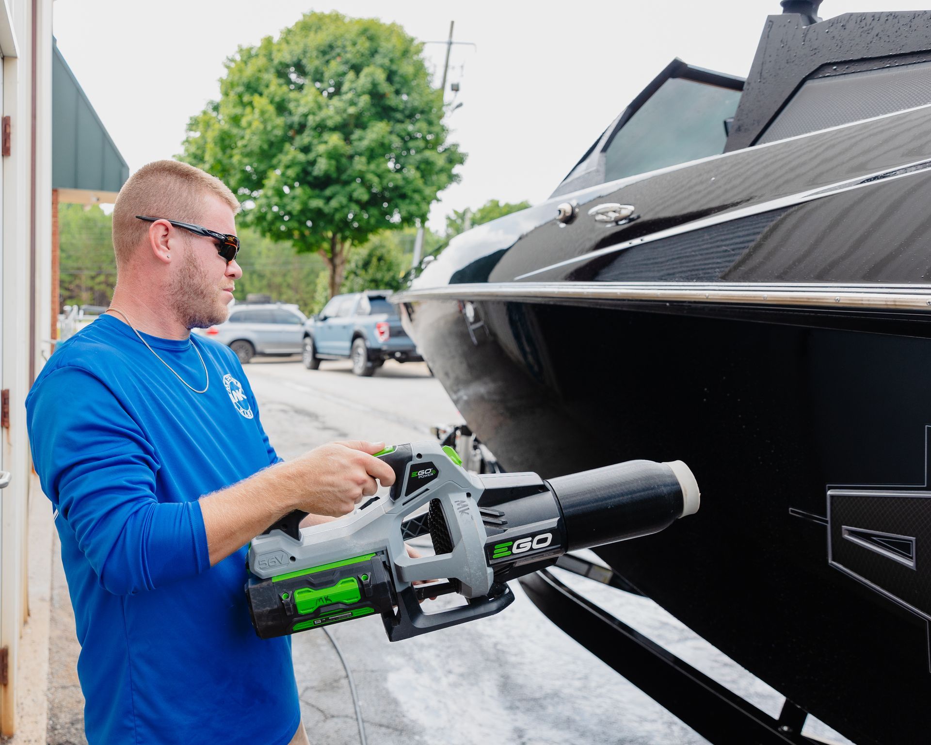 A man in a blue shirt is holding a tool in front of a boat.