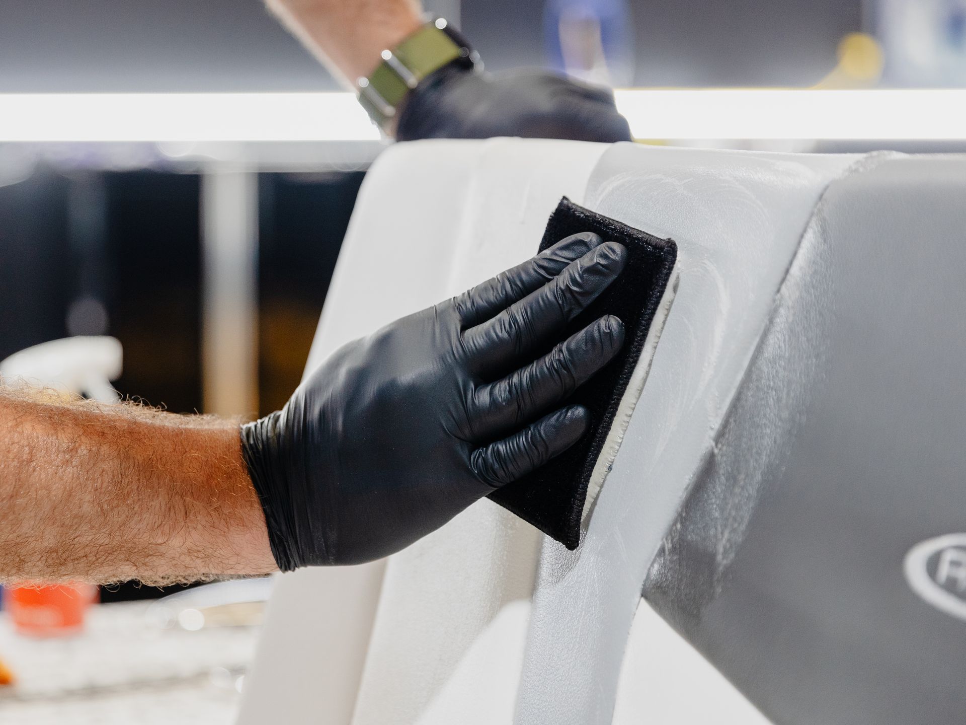 A person wearing black gloves is cleaning a white object with a sponge.