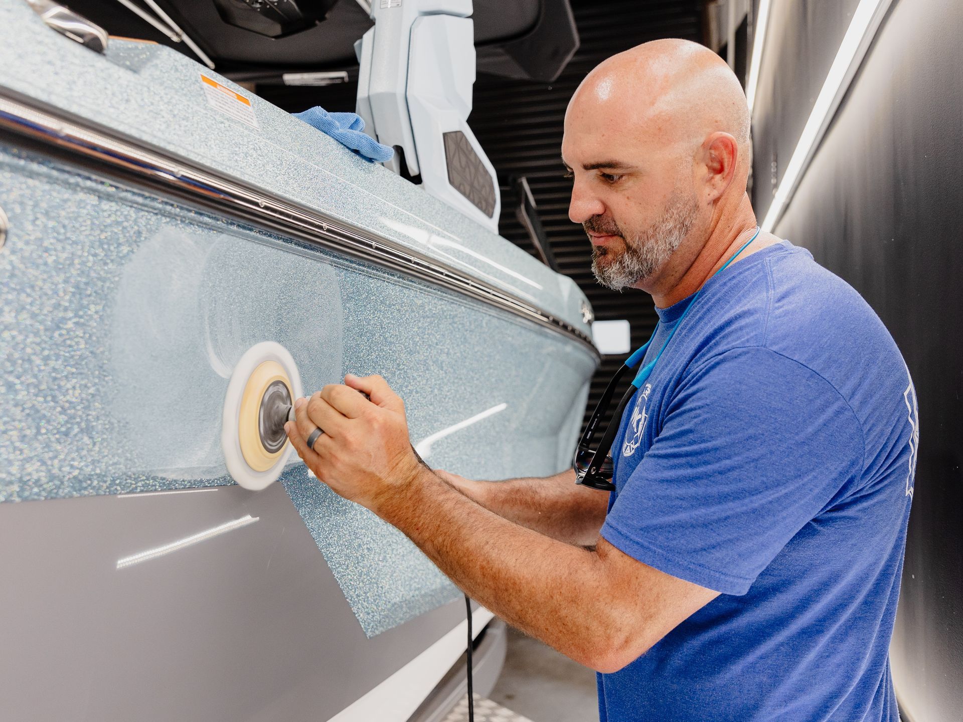 A man in a blue shirt is polishing the side of a boat.