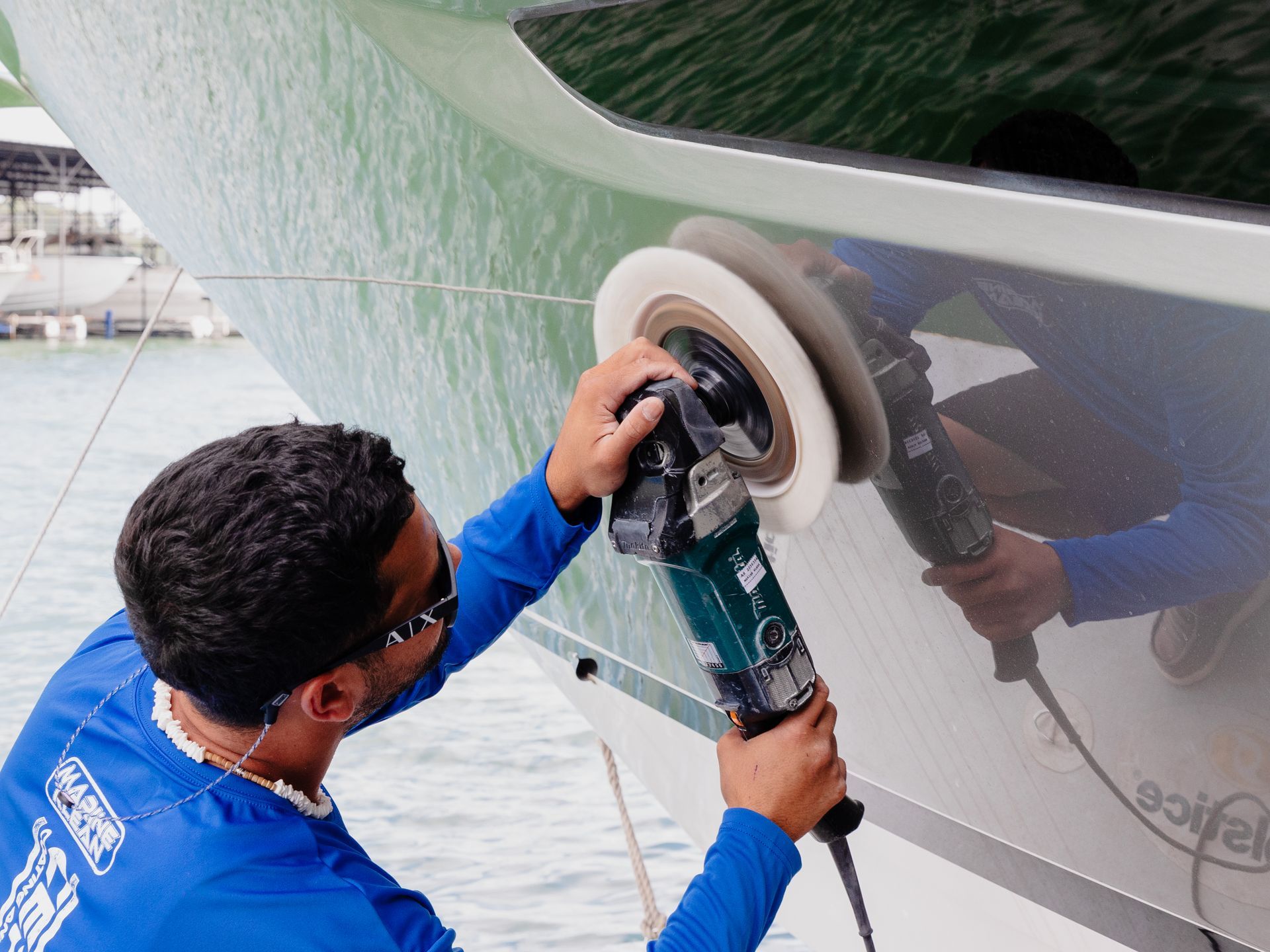 A man is polishing the side of a boat with a machine.