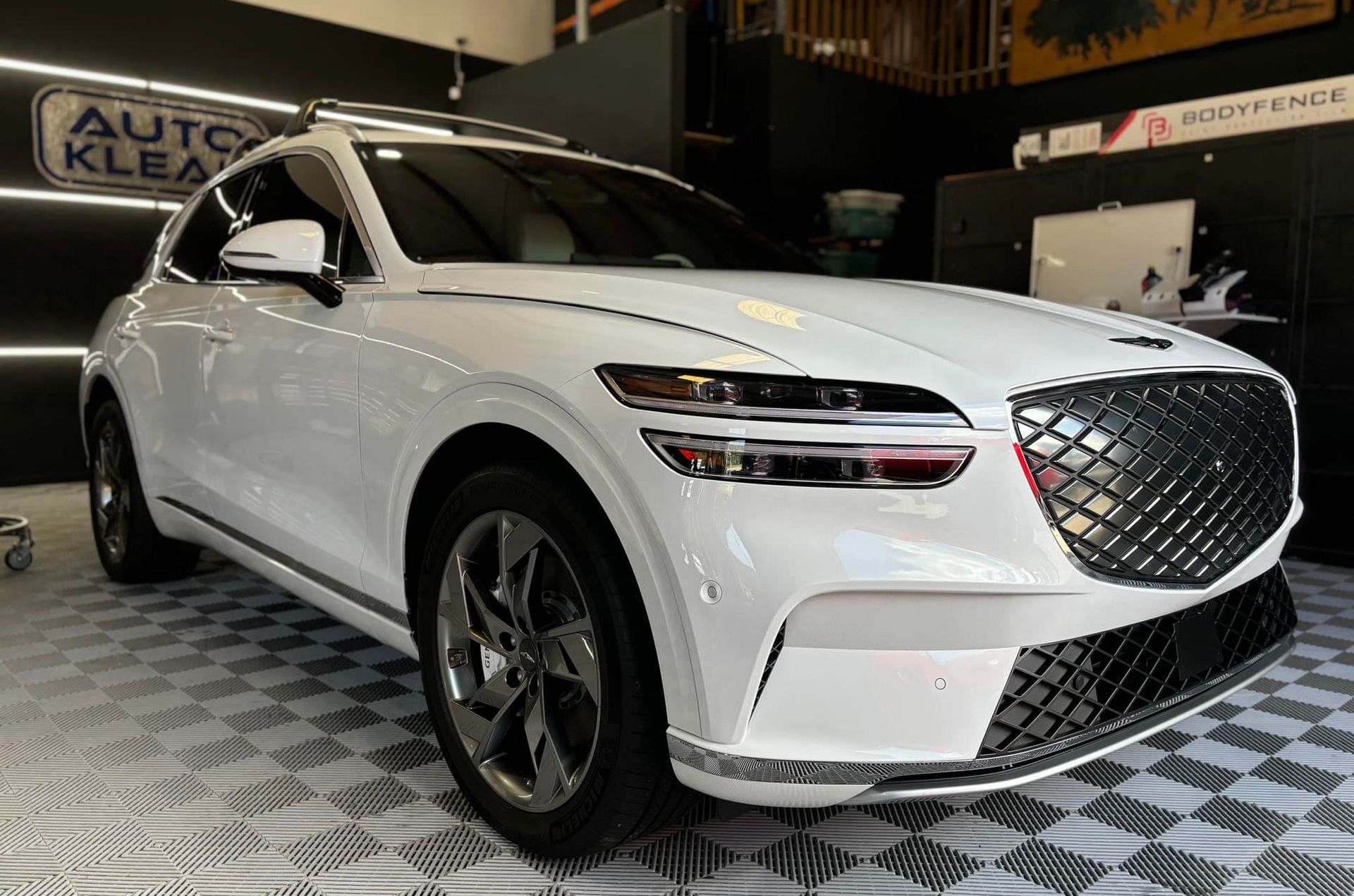 White Genesis GV70 SUV parked in a car detailing shop with black and chrome accents.