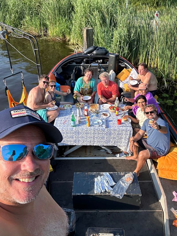 Gezellige rolstoelvriendelijke boottocht in Amsterdam met een BBQ aan boord. Groep mensen geniet van eten en drinken op een toegankelijke rondvaart.