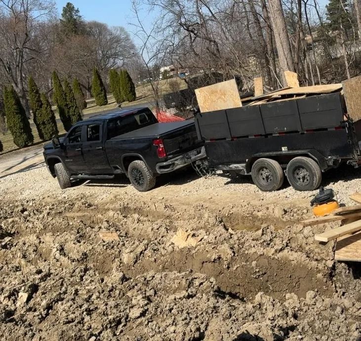 Black truck pulling a trailer loaded with materials on a construction site.