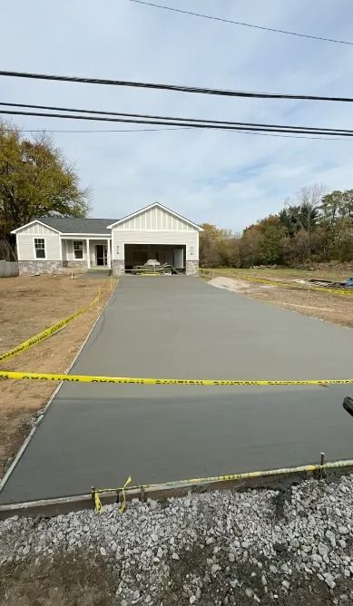 Newly poured concrete driveway leading to a house with a garage; caution tape surrounds the driveway.