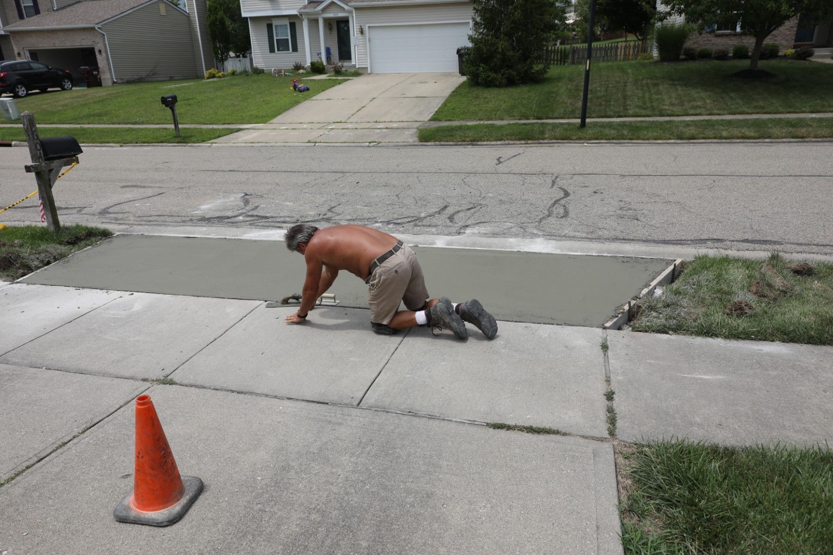 A man is kneeling down on a sidewalk next to an orange cone