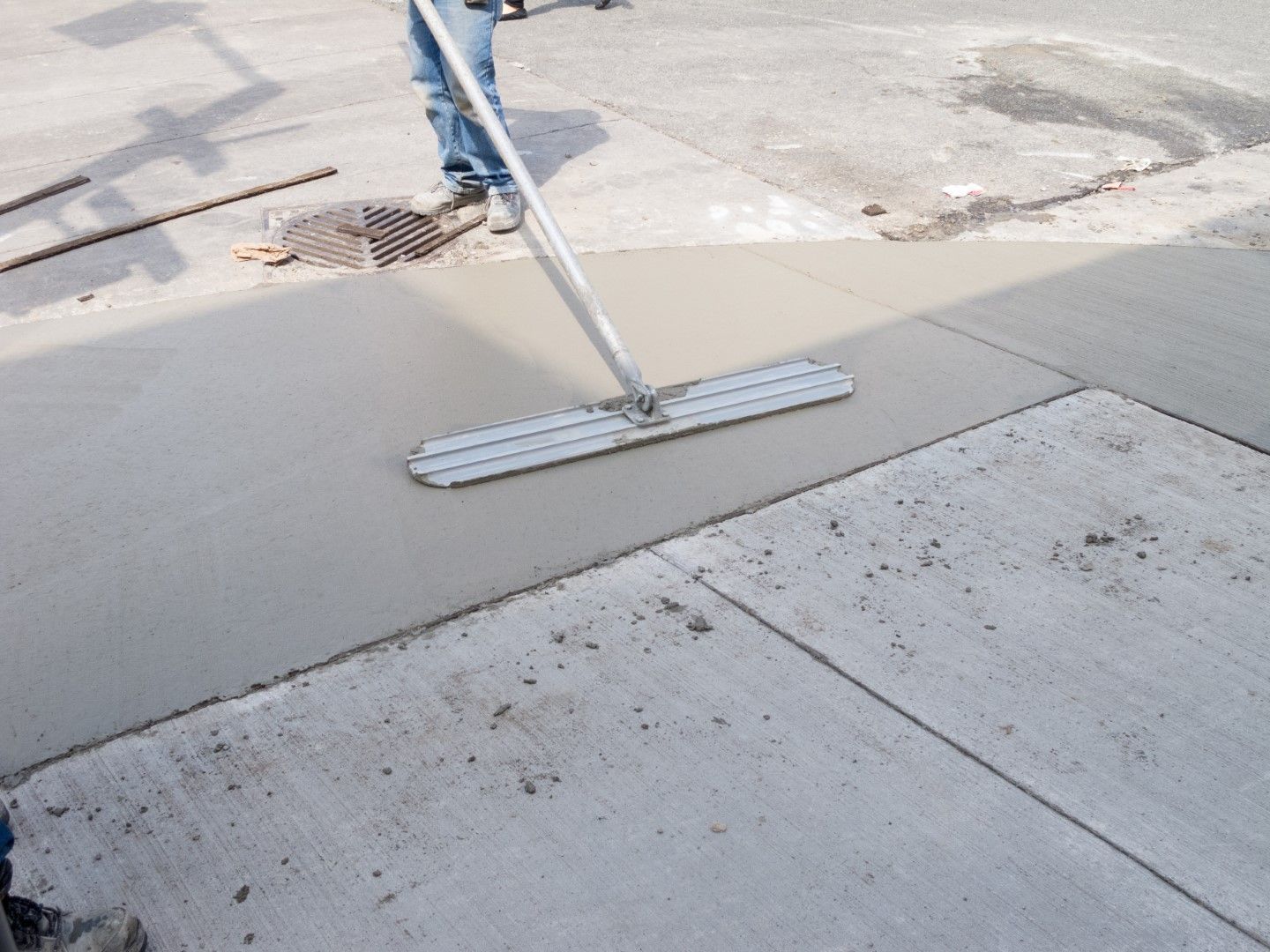 A person is using a mop to spread concrete on a sidewalk
