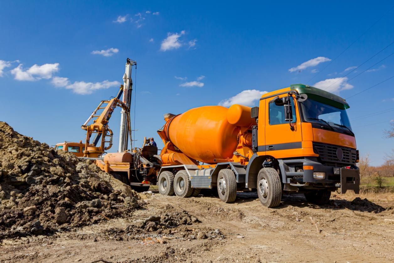 An Orange Cement Mixer Truck Is Parked In A Dirt Field — New England & North West Concrete Pumping In Armidale, NSW