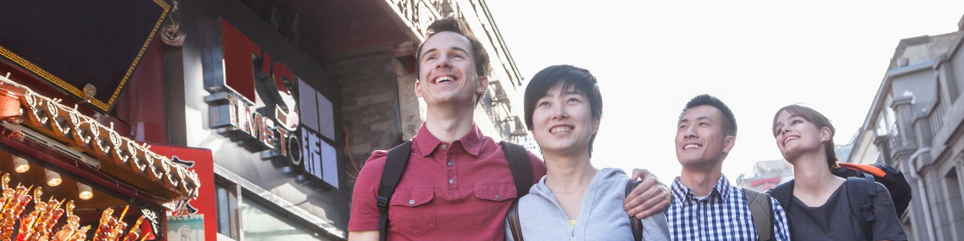 Four people walking and smiling on a sunlit street lined with colorful buildings