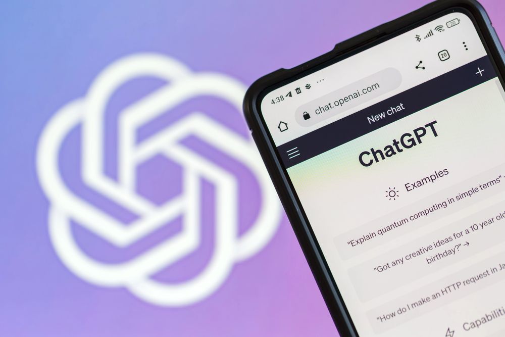 A smartphone displaying the ChatGPT interface is held up in front of the ChatGPT logo on a purple and white gradient background.