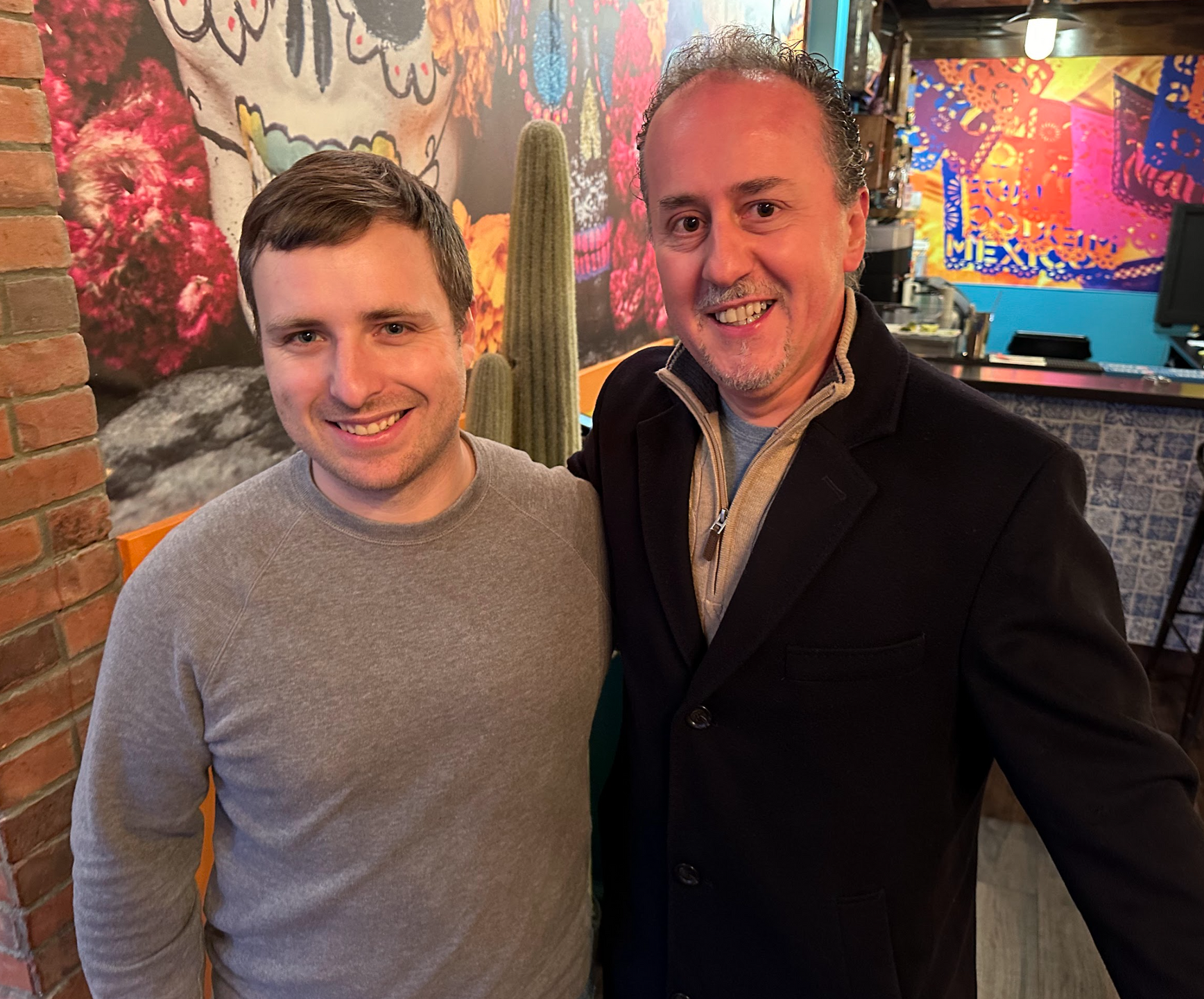 Two men are posing for a picture in front of a wall with a skull on it