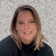 A woman in a black sweater is smiling in front of a silver background.
