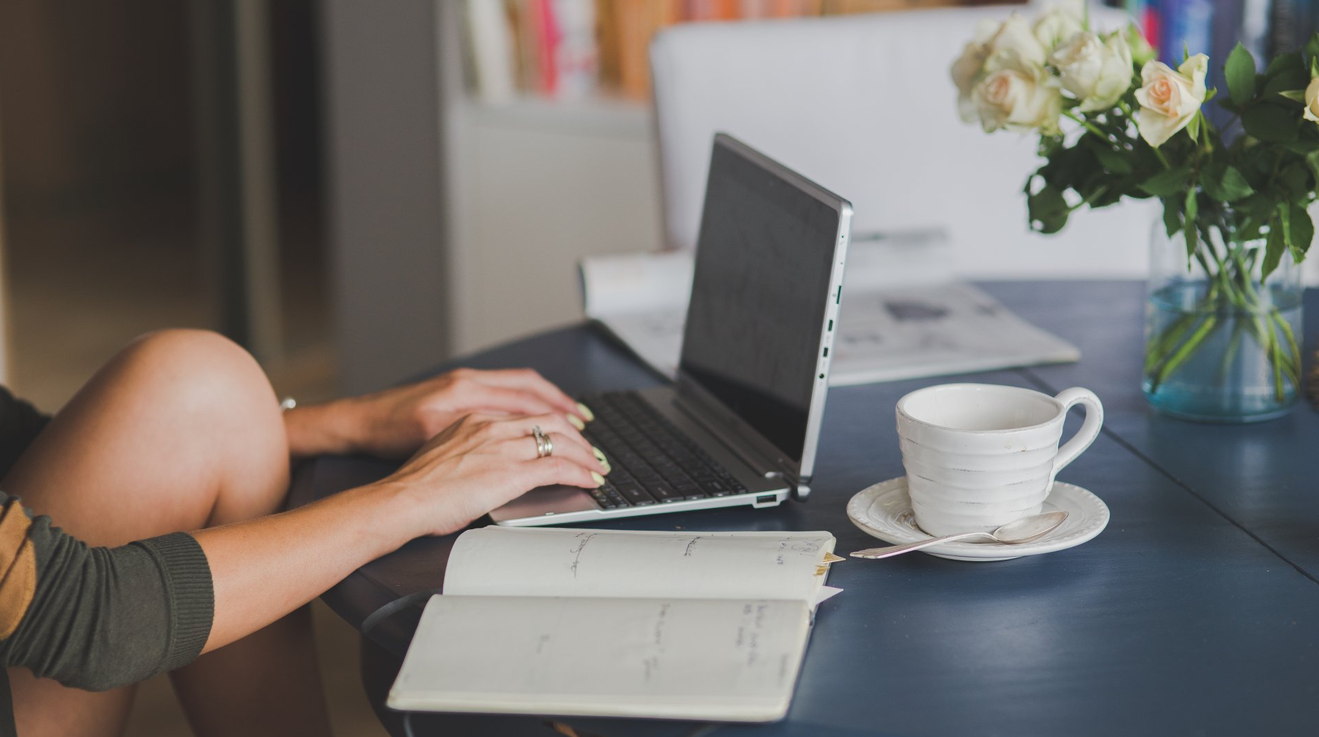 A woman is sitting at a table typing on a laptop computer.