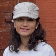 Smiling person in a white cap and T-shirt standing against a red brick wall