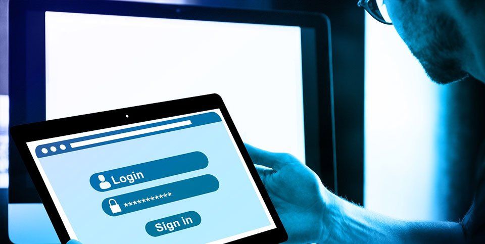 A man is holding a tablet in front of a computer screen.