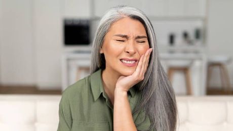 a woman with gray hair is holding her face in pain because of a toothache .