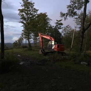 A red excavator is sitting in the middle of a field surrounded by trees.