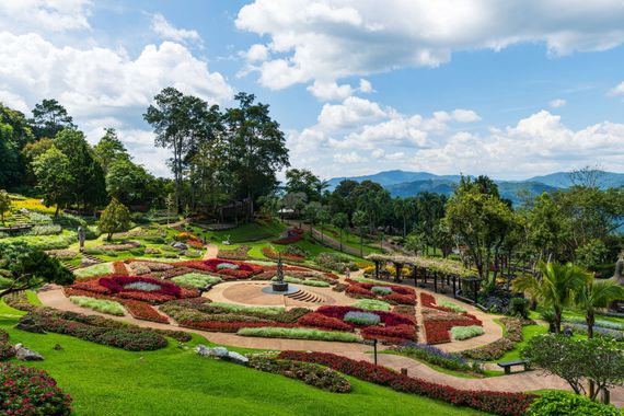 Colorful landscaped garden with flower beds, winding paths, and trees under a blue sky