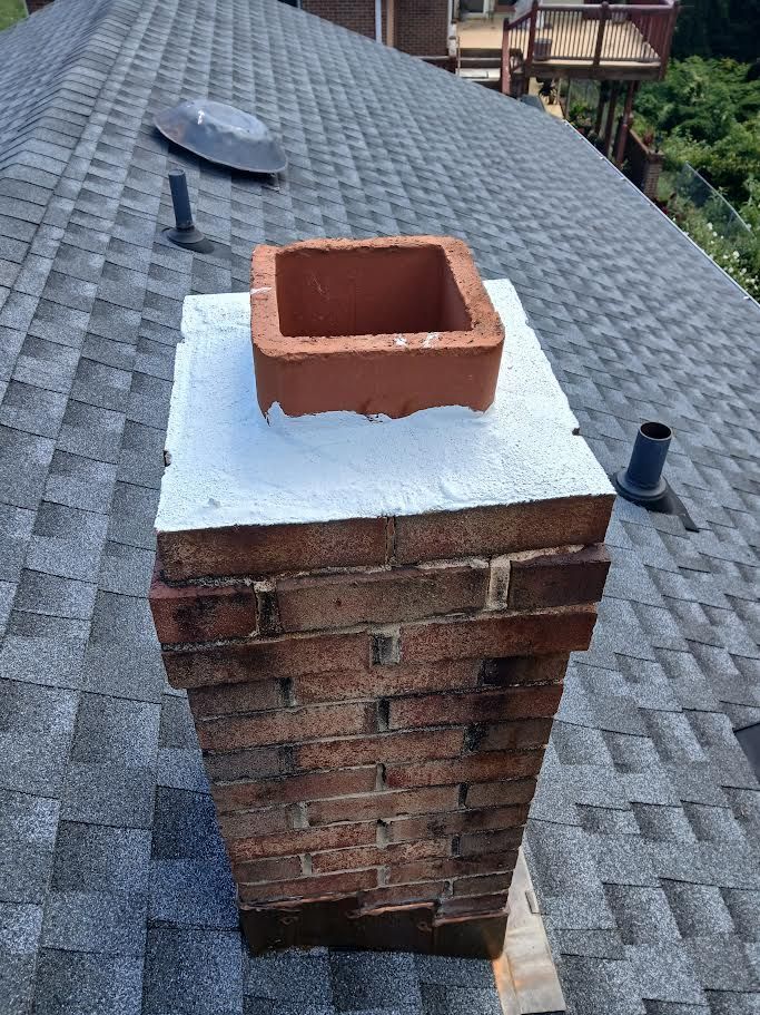 Brick chimney with red flue tile on a shingled roof, capped with white sealant.