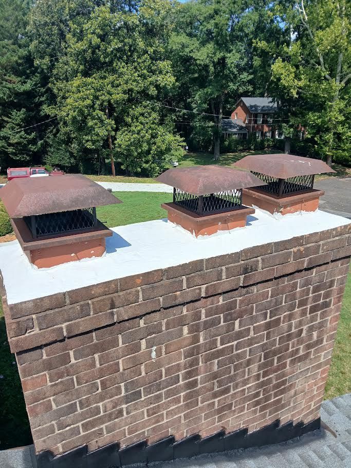 Three small brick chimney caps on a brick rooftop with trees and a house in the background
