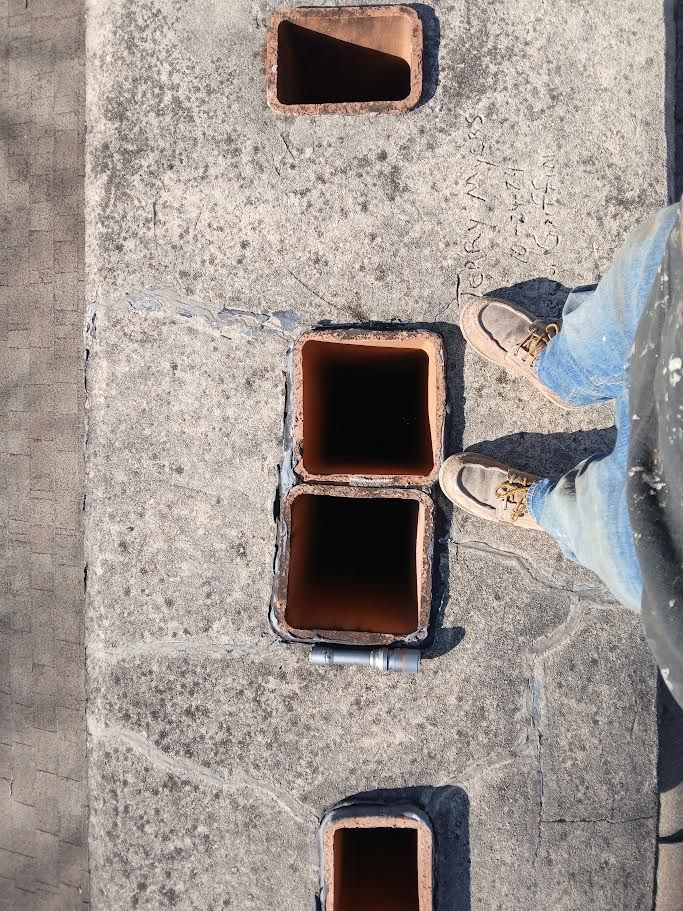 Top-down view of concrete sidewalk with three open rectangular holes and a person’s legs and shoes at right.