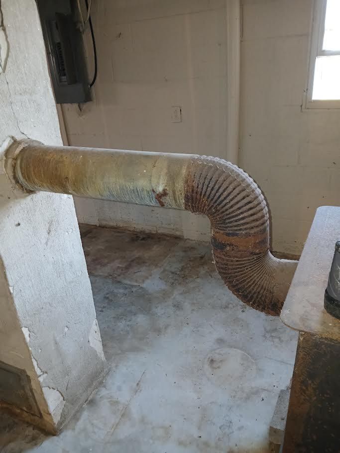 Flexible dryer vent hose through a basement wall, curving to the right near a door.