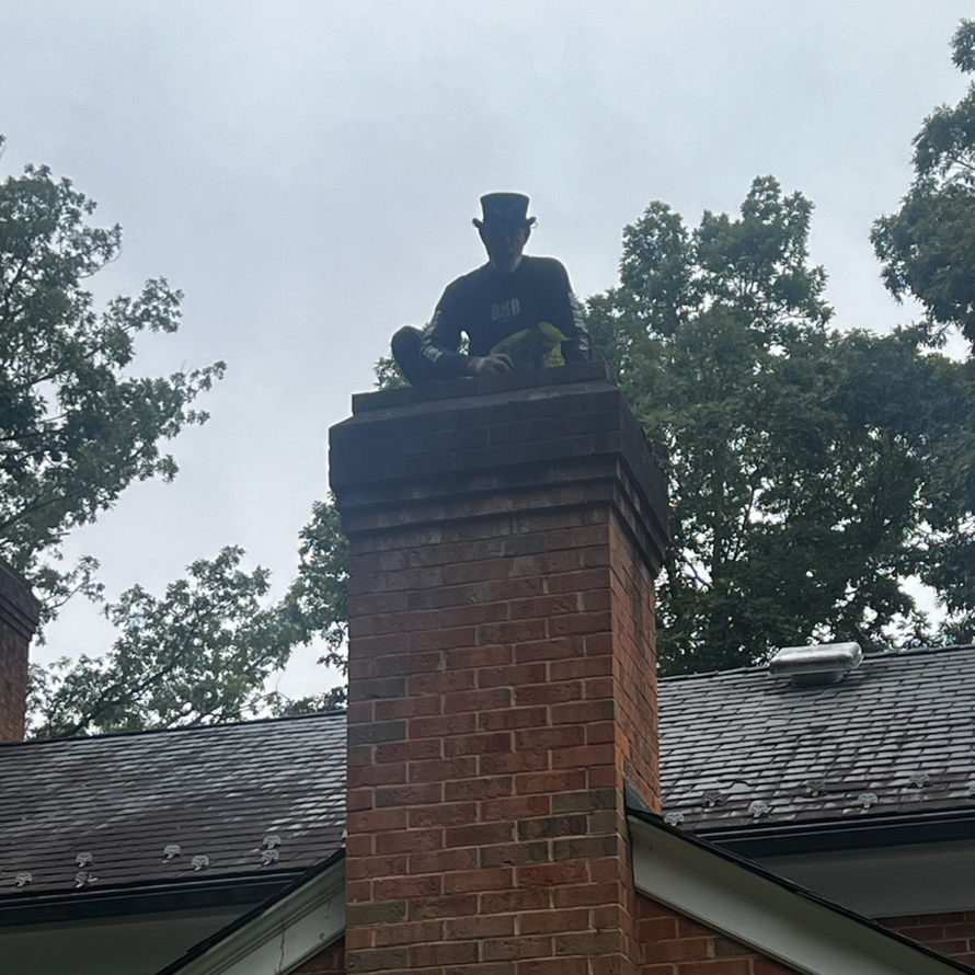 Brick chimney on a metal roof against a blue sky and trees