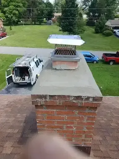 Backyard brick chimney with a metal vent cap and a small solar panel, viewed from a rooftop.
