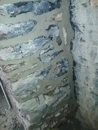 Close-up of a rough, weathered stone or concrete wall with peeling blue-gray paint