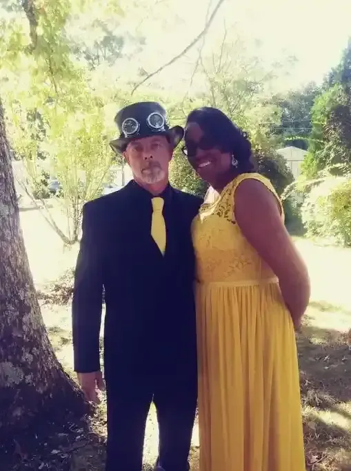 Two people in black and yellow outfits posing outdoors in a sunny garden.