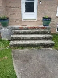 Front steps to a brick house with a white door, flanked by two blue planters and a concrete walkway.