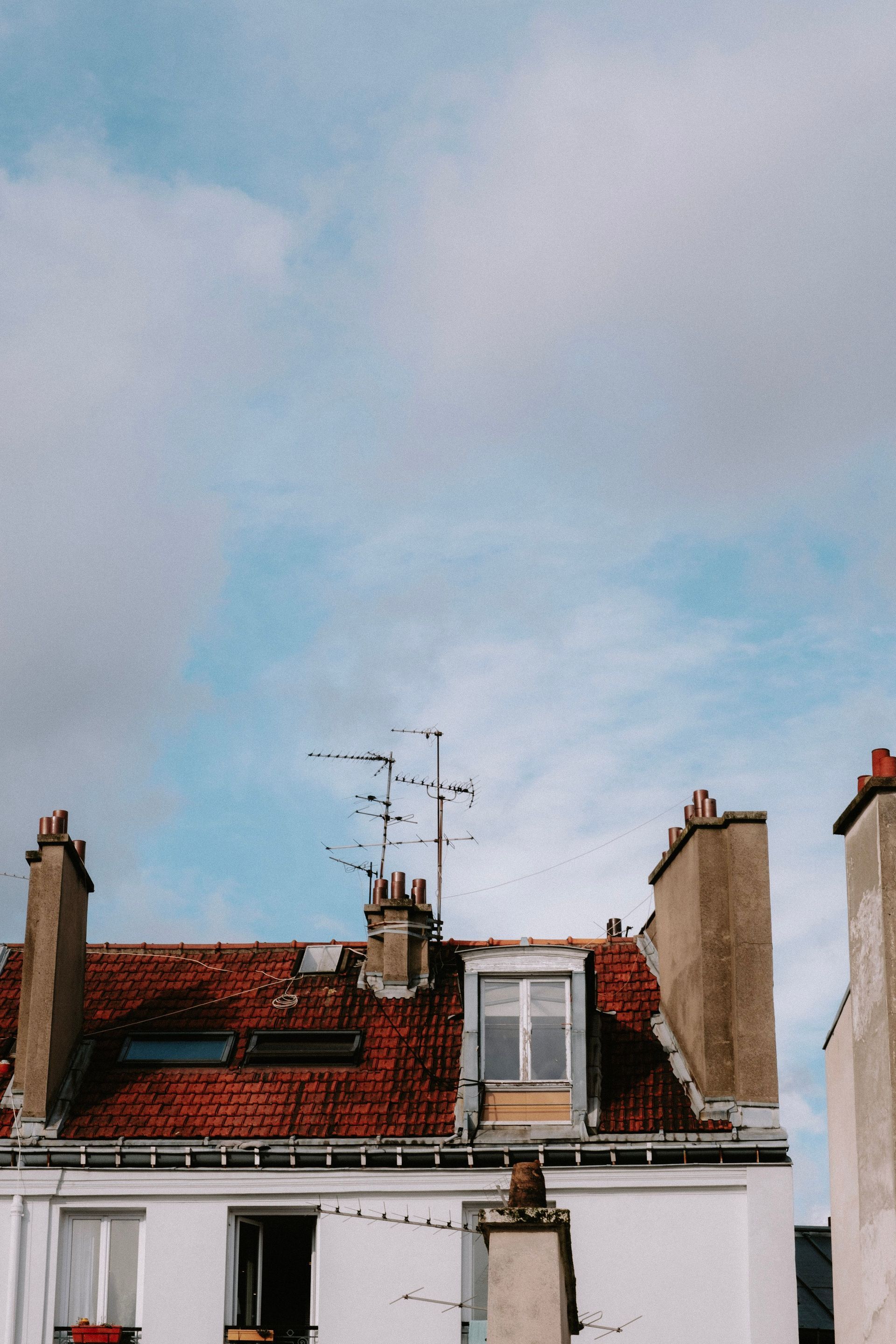 Rooftops with chimneys and TV antennas beneath a cloudy blue sky