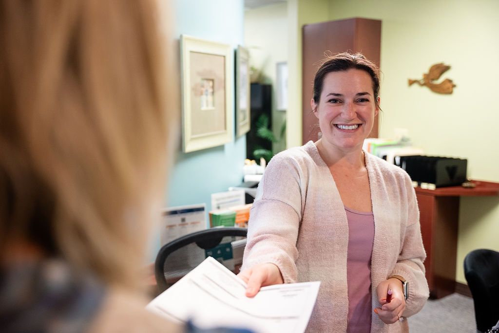 Woman smiling and handing papers across a desk at Robert A. Lantzy, DMD, LCC in Newtown, PA