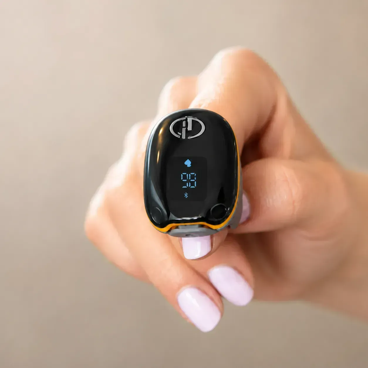 Hand holding a small black digital device with a blue display against a beige background