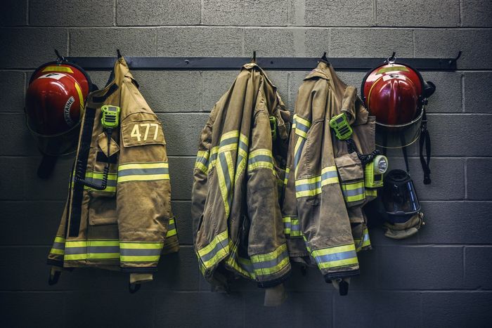 A row of firefighter 's uniforms and helmets hanging on a wall.