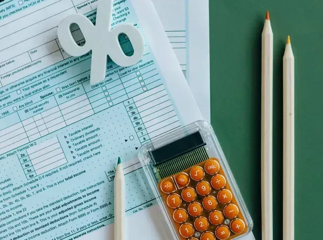A calculator , pencils , and a percent sign on top of a tax form.