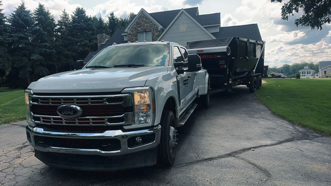 Silver Ford pickup towing a black trailer on a driveway beside a suburban house