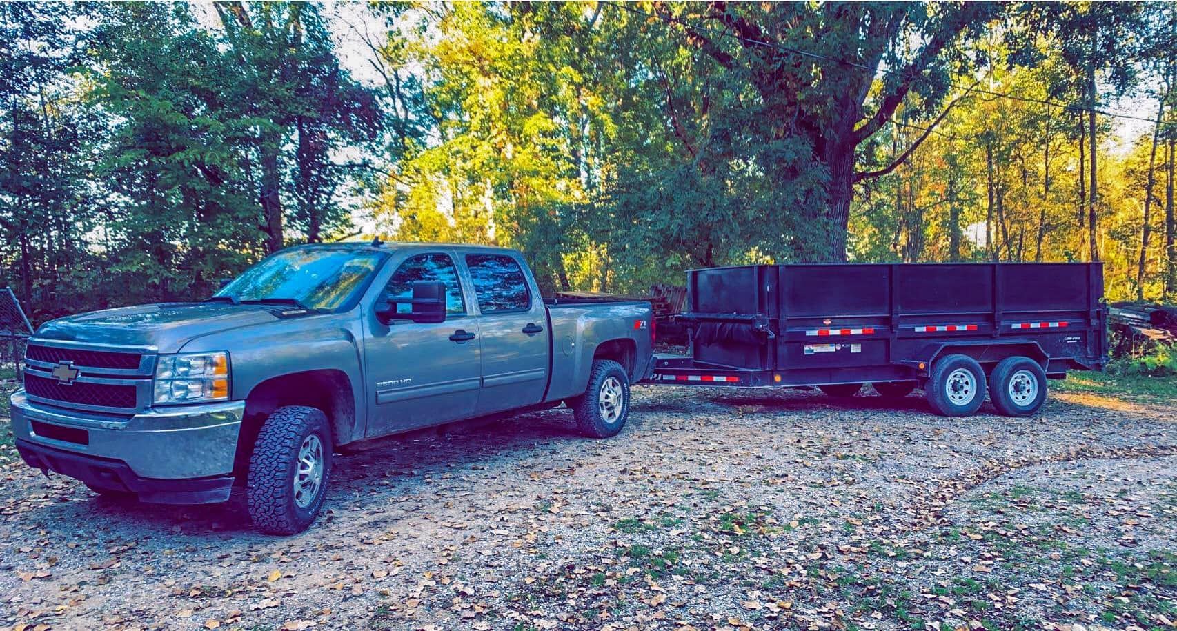Silver pickup truck towing a black trailer on a leaf-covered forest road